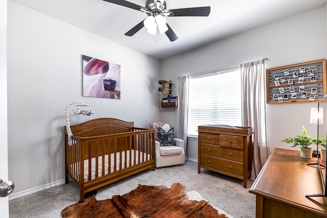 bedroom with a nursery area, light carpet, and ceiling fan