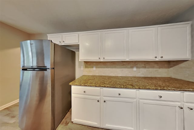 kitchen with white cabinets, tasteful backsplash, dark stone countertops, and stainless steel fridge