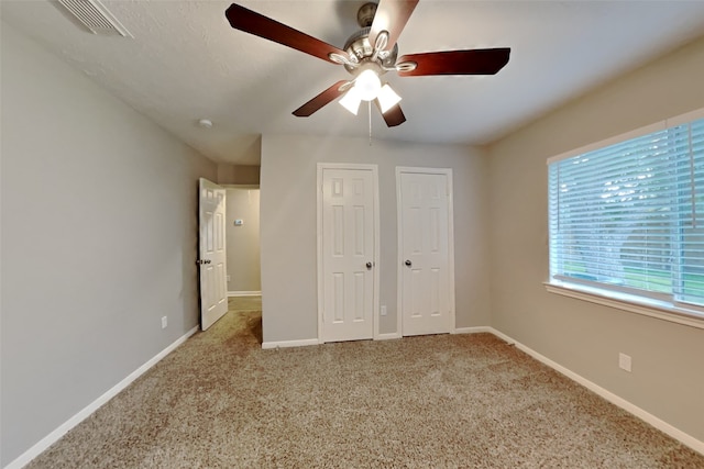 unfurnished bedroom with light carpet, ceiling fan, and two closets