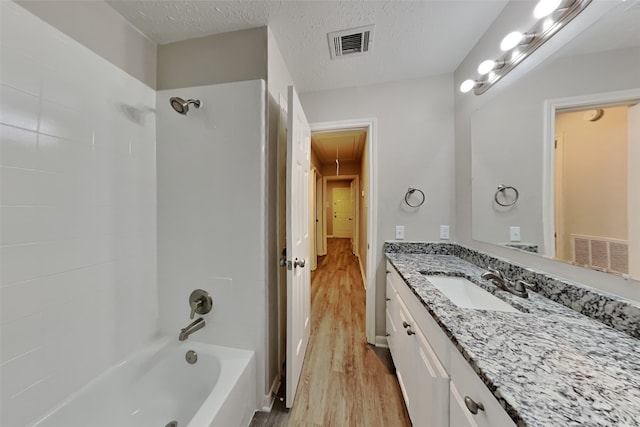 bathroom with wood-type flooring, a textured ceiling, vanity, and bathtub / shower combination