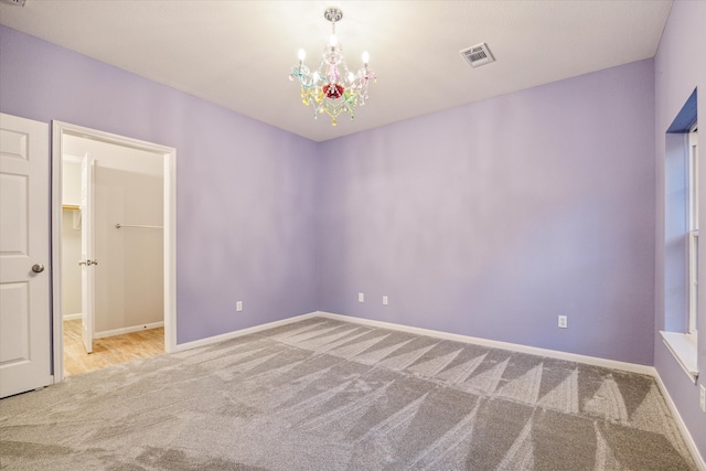 empty room featuring visible vents, light carpet, baseboards, and an inviting chandelier