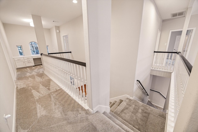 corridor with baseboards, light colored carpet, visible vents, and an upstairs landing