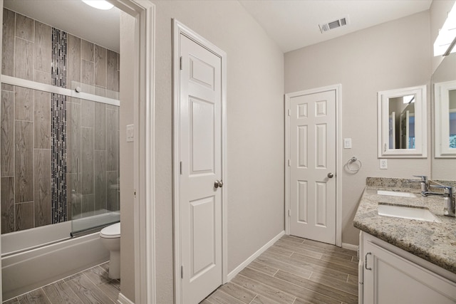 bathroom featuring wood finish floors, combined bath / shower with glass door, a sink, and visible vents