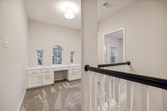 home office featuring baseboards, built in study area, visible vents, and light colored carpet