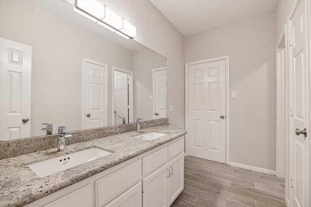 bathroom featuring double vanity, a sink, baseboards, and wood finished floors