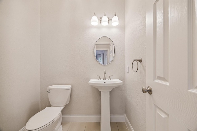 half bathroom with toilet, baseboards, a sink, and tile patterned floors