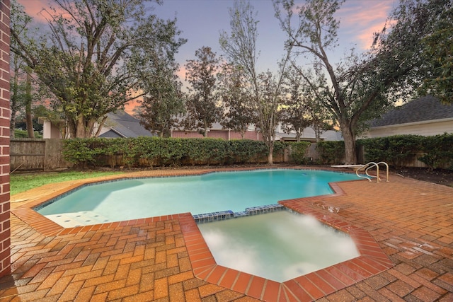 pool at dusk featuring a patio, a fenced backyard, and a pool with connected hot tub