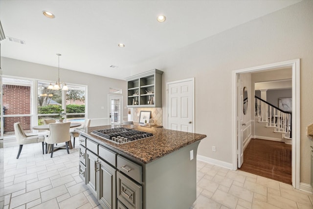 kitchen with dark stone counters, gray cabinets, stainless steel gas stovetop, and hanging light fixtures