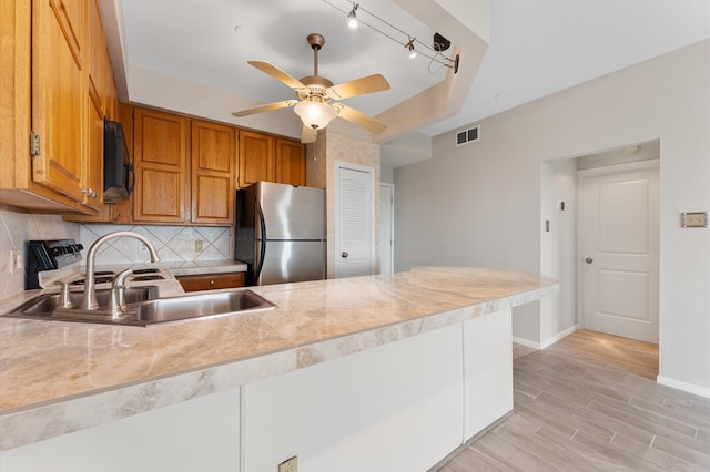 kitchen featuring stainless steel fridge, light wood-type flooring, sink, decorative backsplash, and ceiling fan