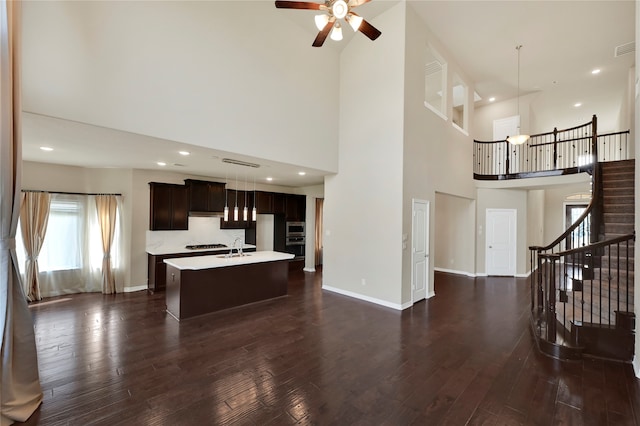 unfurnished living room featuring a towering ceiling, ceiling fan, and dark hardwood / wood-style flooring