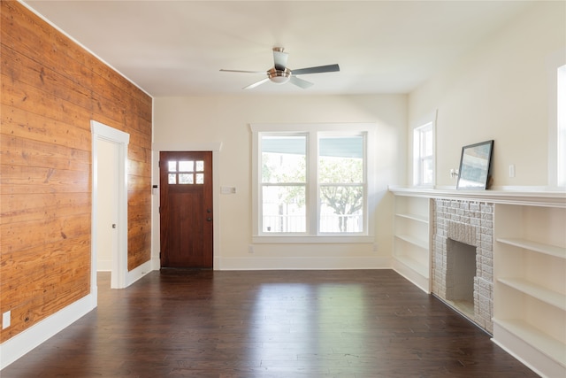 entryway featuring dark hardwood / wood-style flooring, wooden walls, ceiling fan, and a brick fireplace