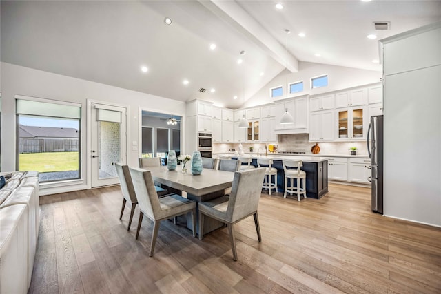 dining room with high vaulted ceiling, beamed ceiling, sink, ceiling fan, and light hardwood / wood-style flooring