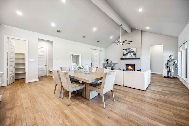 dining area with ceiling fan, high vaulted ceiling, a large fireplace, beamed ceiling, and light wood-type flooring