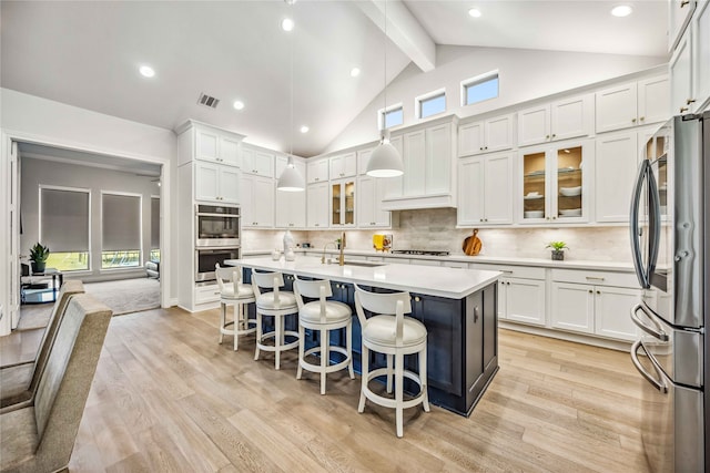 kitchen with appliances with stainless steel finishes, white cabinetry, hanging light fixtures, a kitchen bar, and a center island with sink