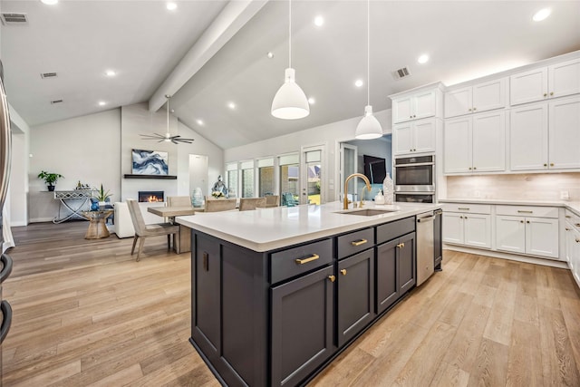 kitchen with a large fireplace, an island with sink, hanging light fixtures, and white cabinets