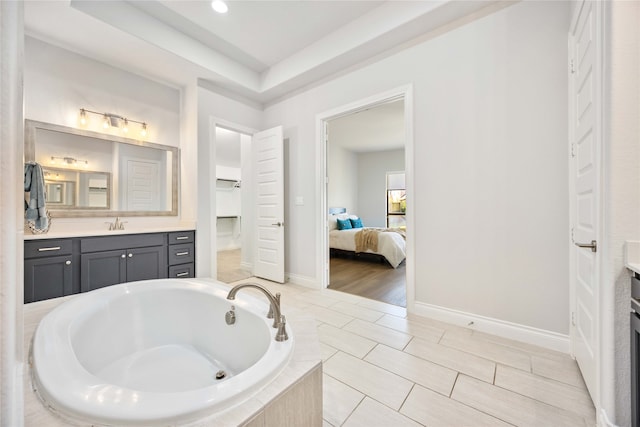 bathroom featuring a relaxing tiled tub, tile patterned floors, vanity, and a tray ceiling