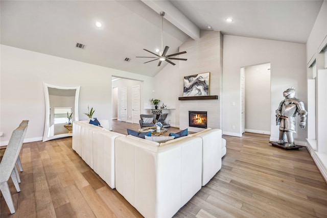 living room featuring beamed ceiling, a large fireplace, ceiling fan, and light hardwood / wood-style floors