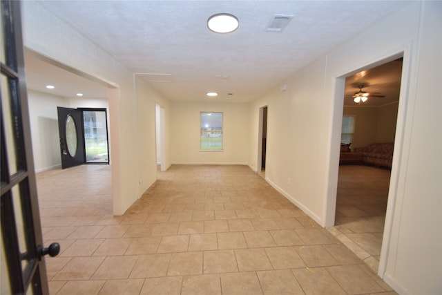 hall featuring a textured ceiling, light tile patterned floors, and a healthy amount of sunlight