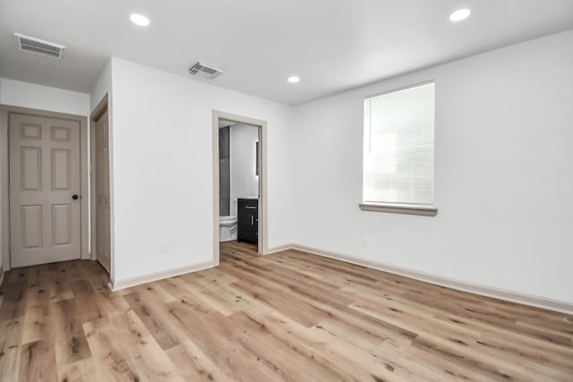 unfurnished bedroom with connected bathroom and light wood-type flooring