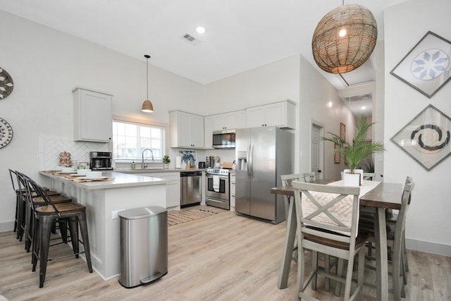 kitchen featuring appliances with stainless steel finishes, hanging light fixtures, tasteful backsplash, white cabinets, and kitchen peninsula