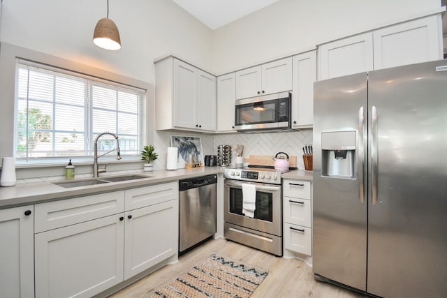 kitchen featuring sink, appliances with stainless steel finishes, white cabinetry, hanging light fixtures, and decorative backsplash