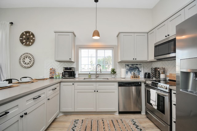 kitchen featuring sink, appliances with stainless steel finishes, hanging light fixtures, decorative backsplash, and light wood-type flooring