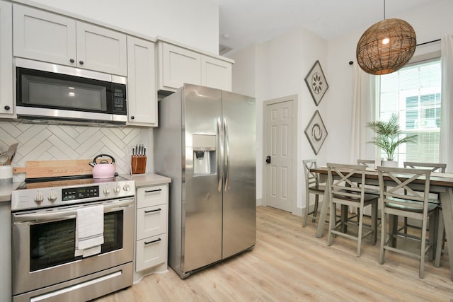 kitchen featuring tasteful backsplash, white cabinetry, light hardwood / wood-style flooring, appliances with stainless steel finishes, and pendant lighting