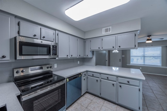 kitchen featuring kitchen peninsula, light tile patterned floors, tasteful backsplash, gray cabinets, and appliances with stainless steel finishes