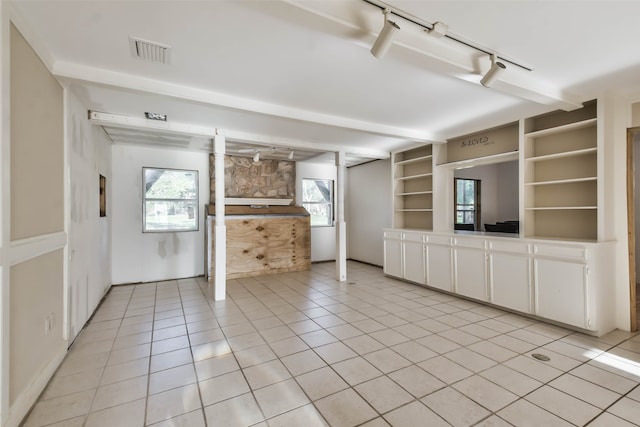 unfurnished living room with beamed ceiling, track lighting, and light tile patterned floors