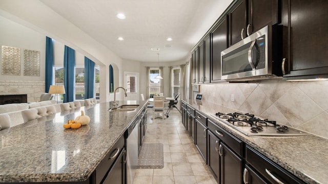 kitchen with tasteful backsplash, stainless steel appliances, a kitchen island with sink, sink, and stone countertops