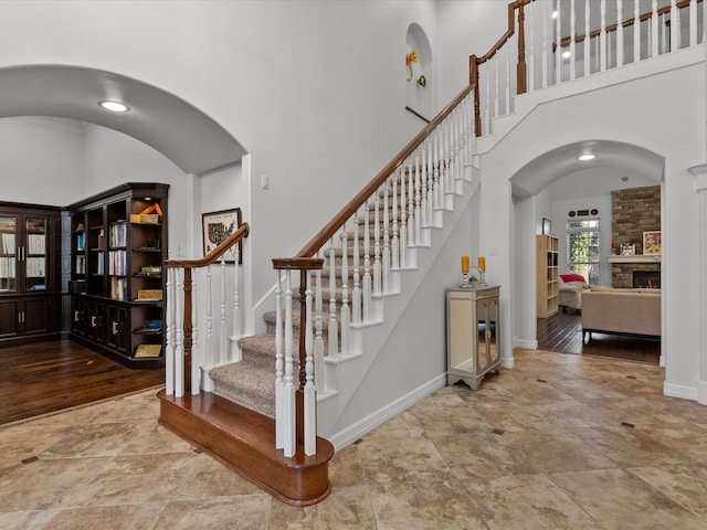 stairway featuring a fireplace, wood-type flooring, and a high ceiling