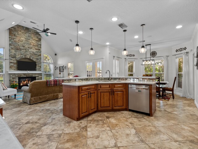 kitchen featuring a stone fireplace, pendant lighting, sink, stainless steel dishwasher, and a kitchen island with sink