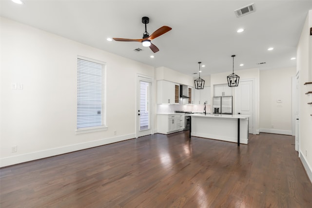 kitchen with pendant lighting, a kitchen island with sink, wall chimney exhaust hood, appliances with stainless steel finishes, and white cabinetry