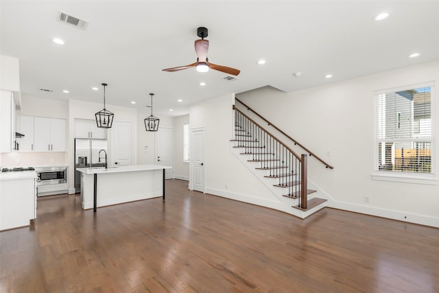 kitchen with ceiling fan, pendant lighting, a center island with sink, dark hardwood / wood-style floors, and white cabinetry