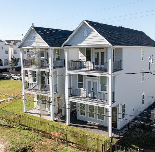 back of property featuring french doors, a balcony, and a lawn