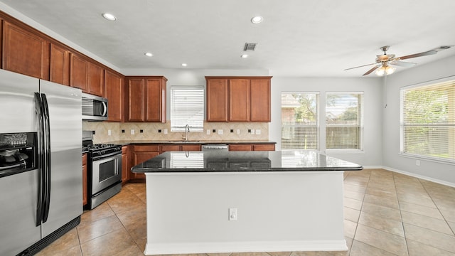 kitchen with stainless steel appliances, dark stone counters, sink, and a center island