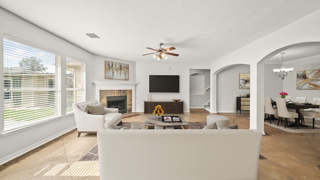 living room with a tiled fireplace, crown molding, and ceiling fan with notable chandelier