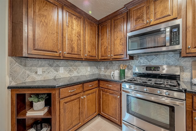 kitchen featuring stainless steel appliances, dark stone countertops, light tile patterned floors, and tasteful backsplash