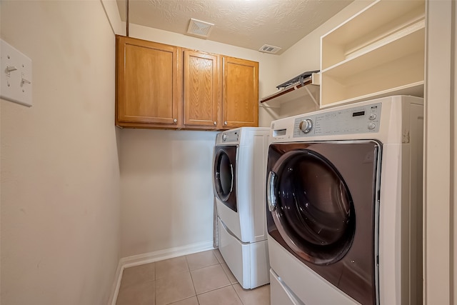 laundry area with cabinets, washing machine and dryer, a textured ceiling, and light tile patterned floors