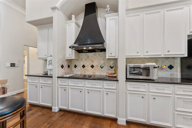 kitchen featuring dark wood-type flooring, black electric cooktop, white cabinets, decorative backsplash, and wall chimney range hood