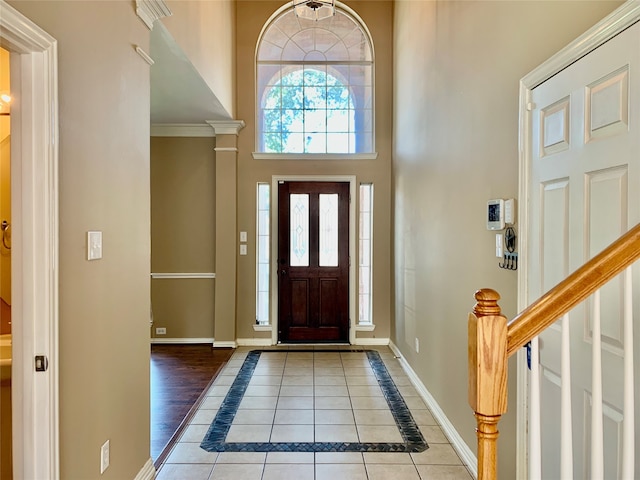 entrance foyer featuring a towering ceiling, decorative columns, wood-type flooring, and crown molding