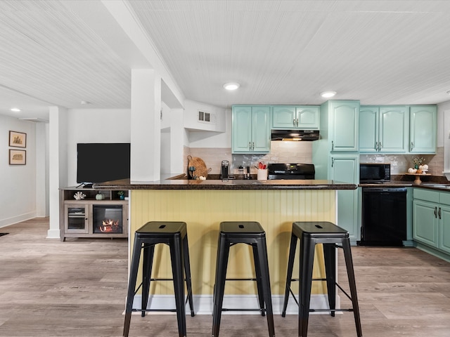 kitchen with a kitchen breakfast bar, black appliances, light hardwood / wood-style flooring, and kitchen peninsula