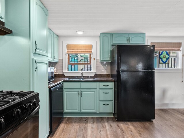 kitchen featuring black appliances, sink, backsplash, green cabinets, and light hardwood / wood-style flooring