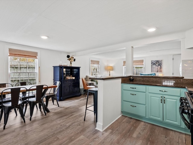 kitchen with wood-type flooring, kitchen peninsula, gas stove, and a breakfast bar