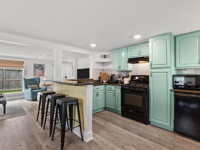 kitchen with green cabinetry, black appliances, decorative backsplash, and a kitchen breakfast bar