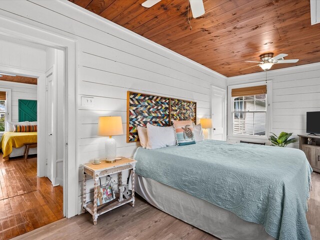 bedroom featuring wood-type flooring, wood walls, and ceiling fan