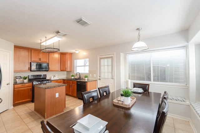 kitchen featuring sink, appliances with stainless steel finishes, light tile patterned floors, decorative light fixtures, and a center island