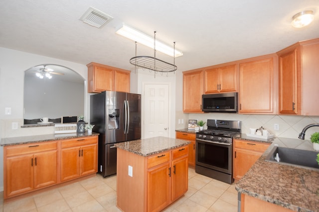 kitchen with light stone counters, stainless steel appliances, sink, ceiling fan, and a center island