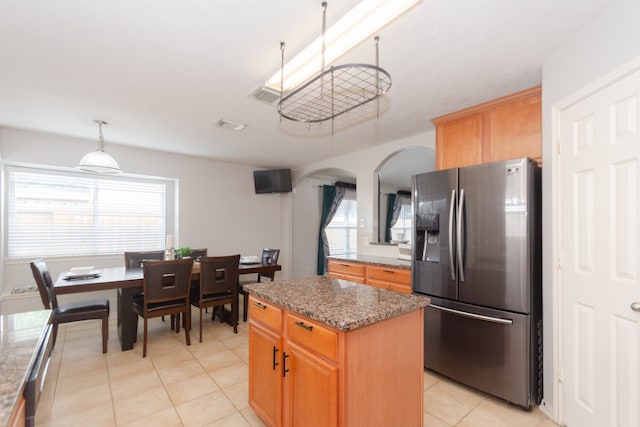 kitchen with a wealth of natural light, stainless steel fridge, dark stone countertops, and a kitchen island