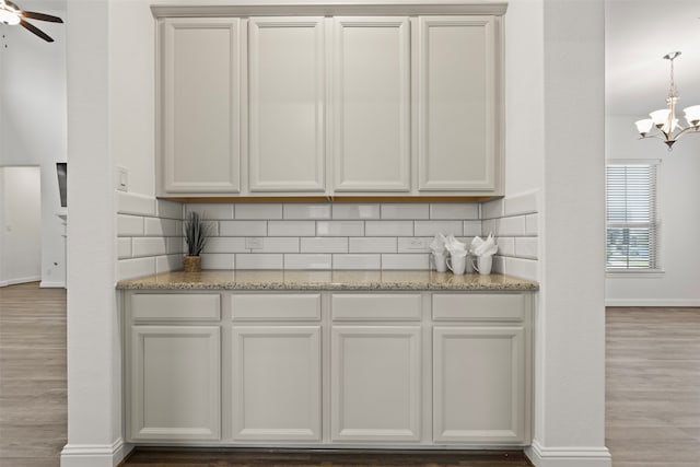 bar featuring light hardwood / wood-style floors, light stone counters, white cabinetry, and tasteful backsplash